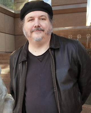 Man with beard and mustache wearing a dark shirt, leather coat, and beret